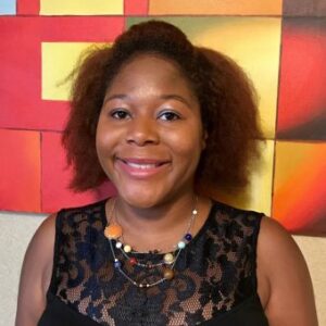 Mahasin Ameen, an African-American woman black dress in front of a red, yellow, and black background.
